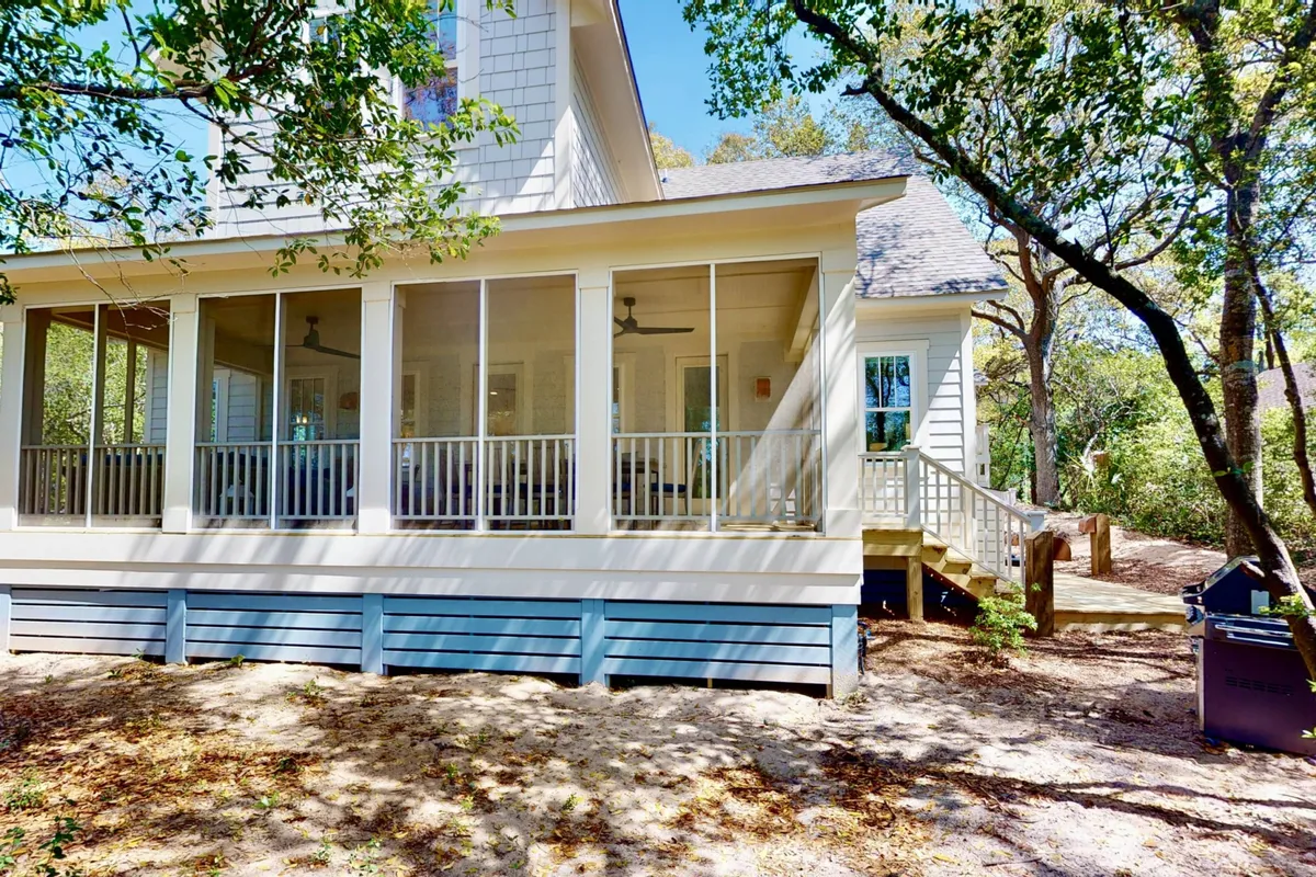 A screened-in porch with wooden steps, surrounded by trees, offers an inviting outdoor extension to the home's entertaining spaces. The area is perfect for alfresco dining, relaxing with friends, or simply enjoying golf course views in comfort.