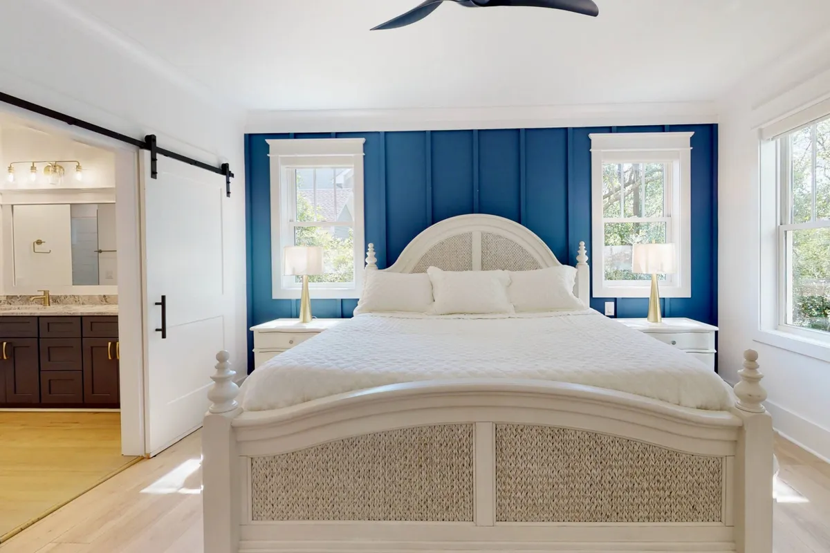 A serene bedroom featuring a king-sized bed adorned with fresh linens, a calming blue accent wall, and nightstands with lamps. The room is bathed in natural light, creating a tranquil retreat perfect for relaxation and restful sleep.