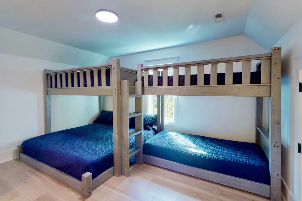 A playful and cozy bunk room with multiple bunk beds, large windows letting in daylight, and textured bedding that invites comfort. The space exudes a sense of fun and flexibility for families or groups, with ample beds for both kids and adults.