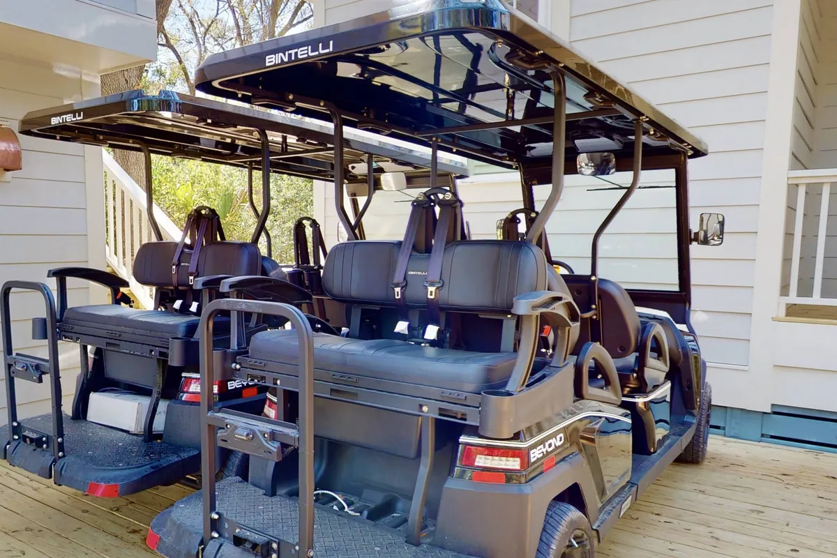 A relaxed outdoor scene featuring golf carts parked on a wooden deck, surrounded by tall trees. The setting suggests easy access to recreational spots and a laid-back island lifestyle, ideal for exploring club amenities or traveling between the house and various club facilities.