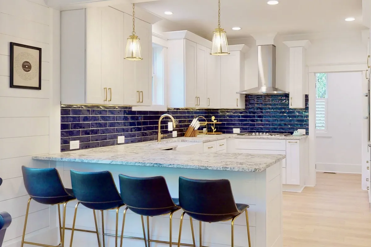 This image showcases the kitchen's island countertop, blue backsplash, gold fixtures, and crisp white cabinetry. The layout emphasizes the kitchen's modern design, with ample workspace, inviting textures, and a central island perfect for communal cooking or casual breakfasts. Various kitchen appliances and gadgets are subtly visible, reinforcing the gourmet appeal.