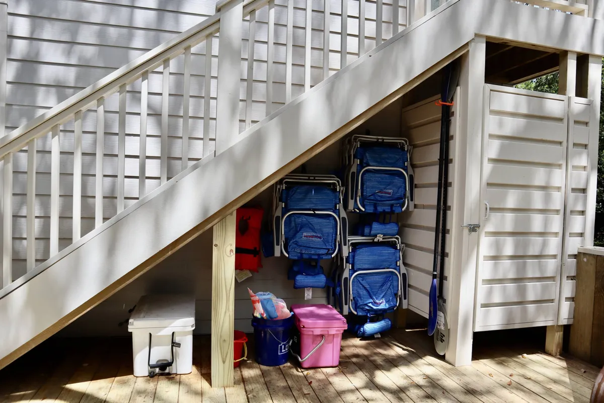 A set of stacked blue beach chairs and a cooler are ready outside a storage shed, signaling easy access to all beach essentials. The casual outdoor setting is tailored for convenience and relaxation.