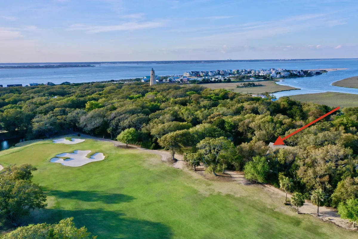 A sweeping view of a scenic golf course bordered by lush trees, with the coastline and a lighthouse visible in the distance. The green fairways stretch toward the water, emphasizing opportunities for outdoor recreation and the unique natural beauty of the island.
