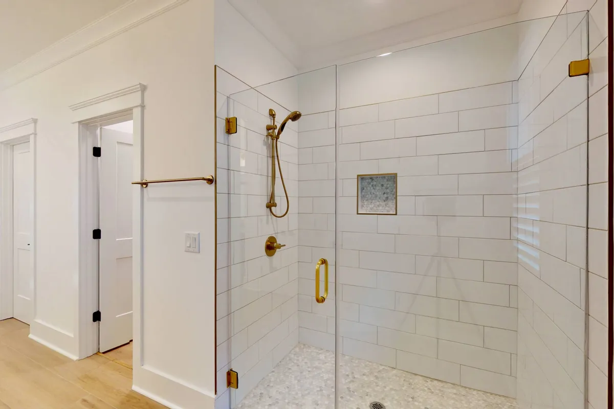 A bright, spa-like interior space with a glass shower enclosure, gold fixtures, and large window. The modern design suggests a refreshing retreat after a day outdoors.
