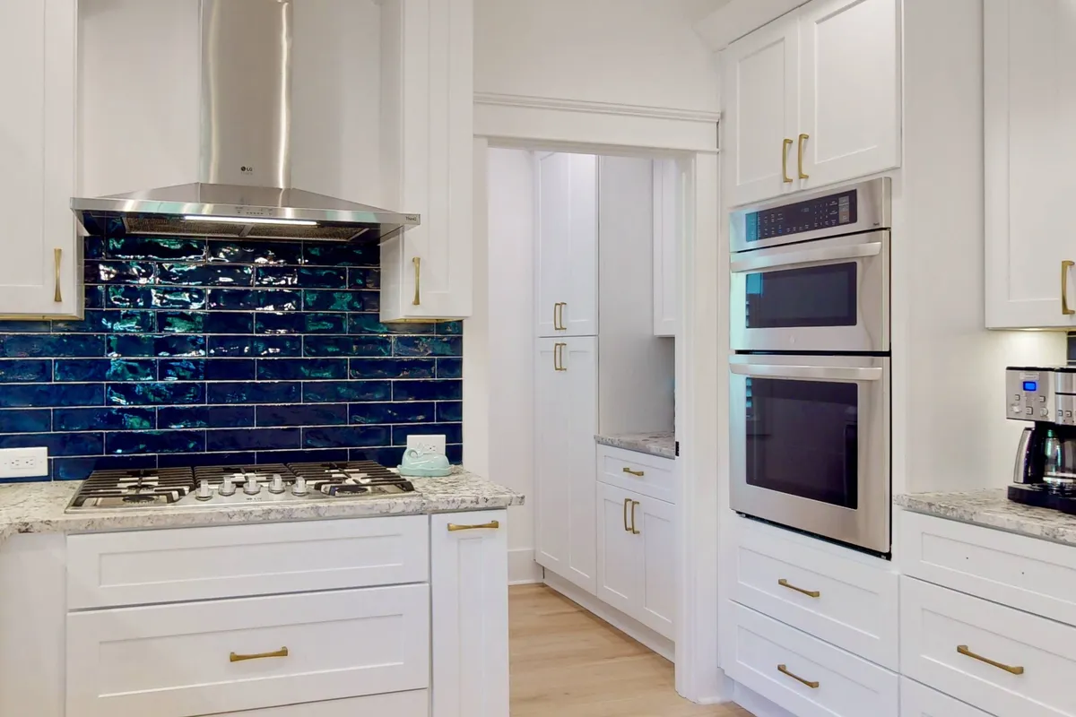 An inviting kitchen interior featuring blue backsplash tiles, stainless steel appliances, and a granite countertop. The space feels fresh and sophisticated, ideal for preparing group meals or hosting casual gatherings when staying in.